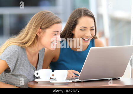 Due amici felice ridere guardare on line il contenuto in un laptop seduto in un ristorante terrazza Foto Stock