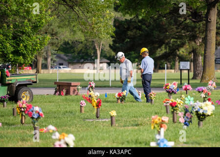 Due dipendenti del cimitero a piedi tra le decorazioni floreali per onorare i morti del Memorial Day in un cimitero di Wichita, Kansas, Stati Uniti d'America. Foto Stock