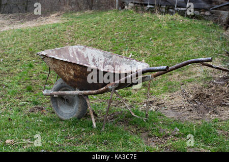 Vecchio e ben utilizzati rusty carriola in un villaggio giardino. Foto Stock