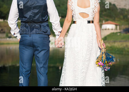 Sposa e lo sposo tenendo le mani di fronte a un lago Foto Stock