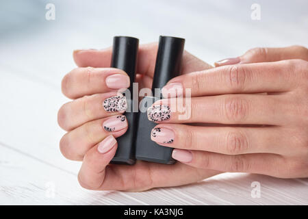 Bottiglie di chiodi polacco in mani femminili. womans mani con caldi beige manicure con due contenitori di smalto per unghie. scelta il design e il colore di Foto Stock