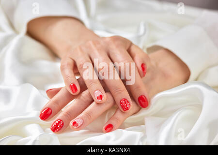 Femmina design romantico manicure. giovane donna ben curati con le mani rosso chiodi modellato su bianco seta. pulizia femminile e delicatezza. Foto Stock