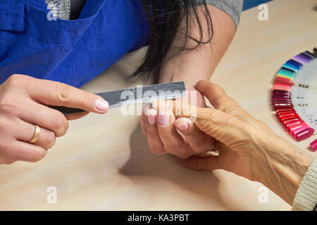 Estetista unghie di deposito a cliente. donna mani in manicure ricevendo manicure. vecchia donna sta diventando manicure in un salone di bellezza. Foto Stock