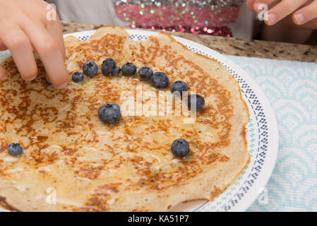 Close-up del bambino la mano la preparazione di crepes con mirtilli e miele. Foto Stock