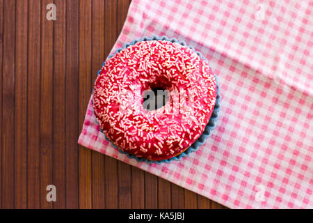 Luminosamente ciambella rosa su di un legno marrone. sfondo rosa con panno a scacchi Foto Stock