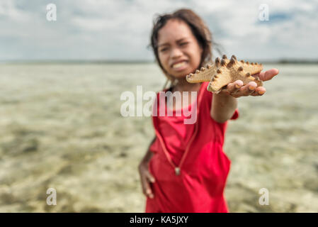 Bambina gioca con starfish in Semporna mare Foto Stock