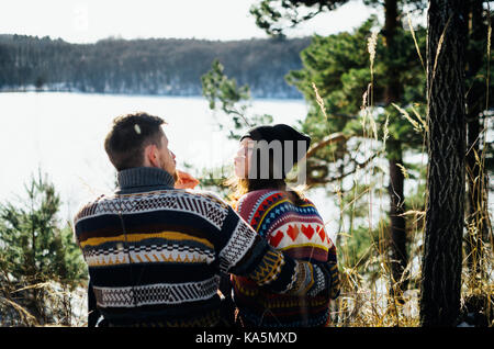 Gioiosa funny giovane in vestiti caldi di fronte lago ghiacciato tra foresta. giovane uomo abbraccia la donna. il concetto di rapporto di successo e felice Foto Stock