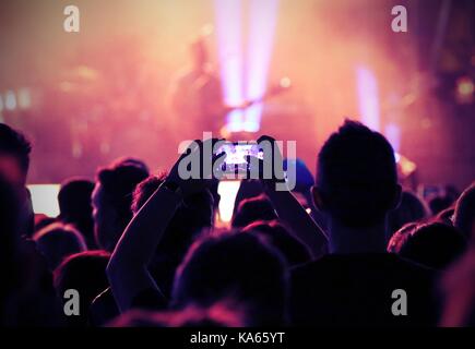 Giovani fan scatta una foto il chitarrista sul palco durante un concerto dal vivo Foto Stock