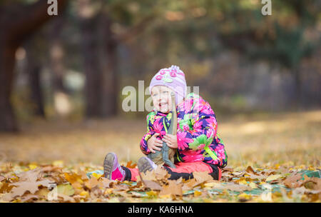 Felice bambina gioca con il giocattolo dinosauro nel parco di autunno Foto Stock