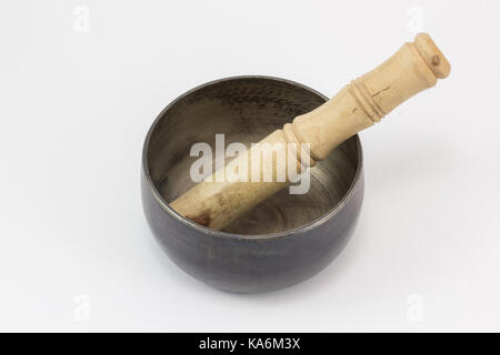 Un Singing Bowl, fatta di metallo, e un bastone di legno in essa, su una superficie bianca. Foto Stock