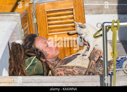 Donna con tatuaggi posa su una barca sotto il sole con un cane. Foto Stock