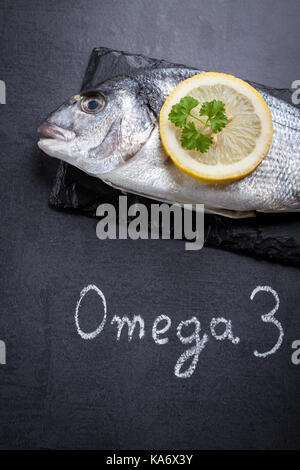 Materie dorada pesce che posa in ardesia nera e parola scritta omega 3 dal gesso bianco. Foto Stock