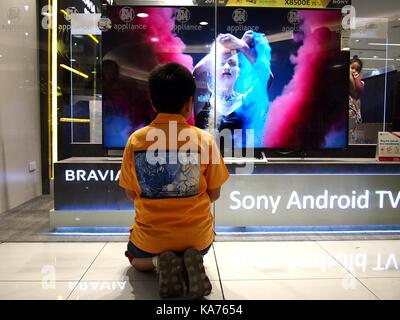 Mandaluyong city, Filippine - 24 settembre 2017: un giovane ragazzo tv orologi al di fuori di un negozio di elettronica. Foto Stock