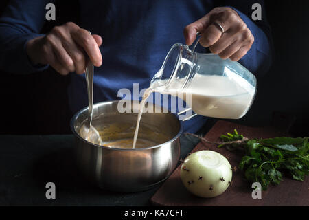 Il latte dalla caraffa è versata in una salsa di base per la realizzazione di besciamella in orizzontale Foto Stock