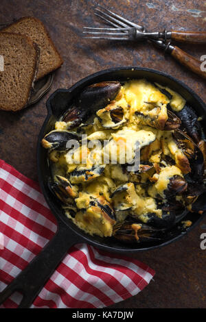 Cozze con salsa al formaggio in una padella, un tovagliolo in una gabbia rossa verticale Foto Stock