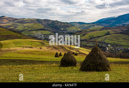 Haystacks sul prato erboso in autunno le montagne. villaggio e la ferrovia può essere visto in giù nella valle Foto Stock