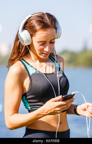 Giovane donna sportivo utilizza lo smartphone sulla formazione . sorridente ragazza con le cuffie per ascoltare musica all'aperto allenamento in mattinata estiva Foto Stock