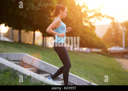 Sorridente giovane donna sportivo scendendo su scale di formazione nella mattina. Idoneità ragazza di andare giù per le scale a fare jogging nel parco Foto Stock