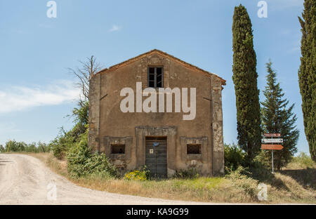 Toscana-giugno 1: casa abbandonata con alberi accanto a una strada di campagna in Val d' Orcia,Toscana,l'Italia,su giugno 1,2017. Foto Stock