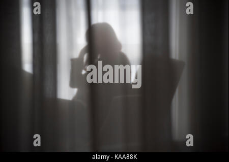 Silhouette di una ragazza dietro una tenda bianca Foto Stock