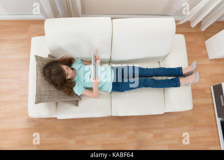 Angolo di alta vista della ragazza distesa sul divano con tavoletta digitale in salotto Foto Stock