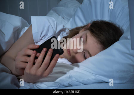 Ragazza sms sul cellulare durante la notte mentre giaceva a letto Foto Stock