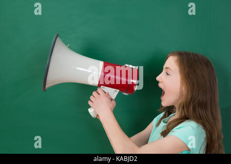 Ragazza annunciando il megafono contro la lavagna in aula Foto Stock