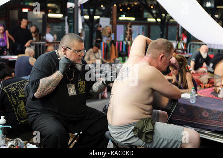 L'uomo ottenendo la sua schiena tatuata presso la London International Tattoo Convention 2017, Tabacco Dock, Londra, Regno Unito. Foto Stock