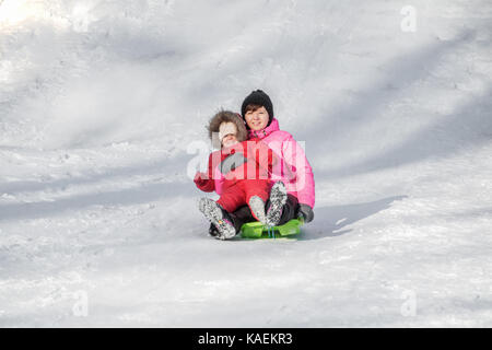 Felice madre e figlia godendo di un giro in slitta verso il basso le colline, inverno giochi e divertimento. vacanze in famiglia e di stare insieme. Foto Stock