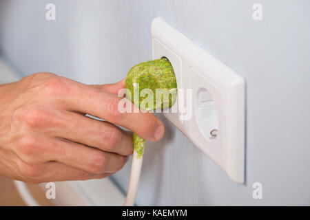 Primo piano della mano verde di inserimento della spina elettrica in una presa a muro Foto Stock
