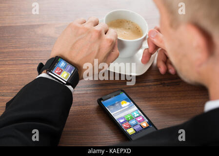 Close-up di imprenditore con smartphone e smartwatch holding tazza di caffè sulla scrivania Foto Stock