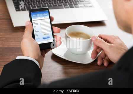 Close-up di un imprenditore in cerca di lavoro sotto forma di applicazione sul cellulare mentre un caffè Foto Stock