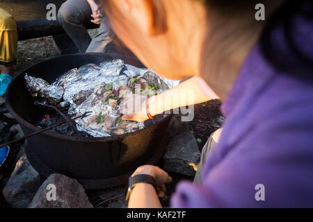 Donna matura la cottura alla griglia di cibi in firepit al forest Foto Stock