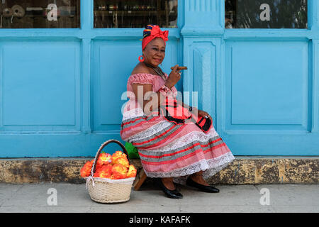 Un colorfully vestito donna cubana in abiti tradizionali si siede sulle strade di Habana vieja a l'Avana, Cuba. Foto Stock