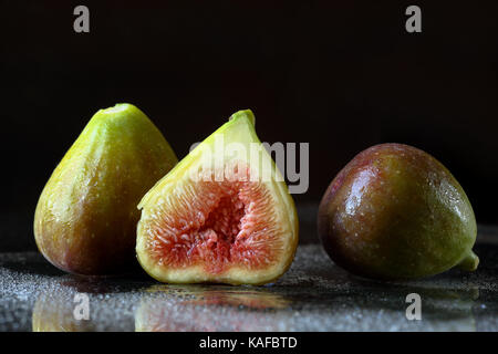 Chiudere fino a due e una metà fresche a fette fig la frutta in un umido sfondo nero con riflessi e gocce d'acqua. Macro food texture con spazio per il testo Foto Stock