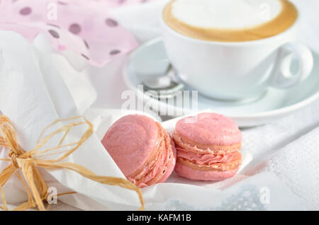 Due macarons rosa con una tazza di cappuccino Foto Stock