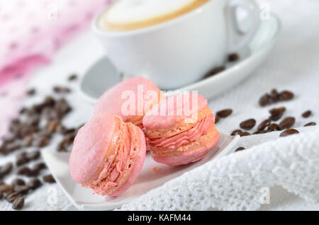 Tre macarons rosa con una tazza di cappuccino Foto Stock