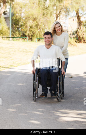 Uomo disabili su sedia a rotelle a piedi con la sua ragazza nel parco Foto Stock