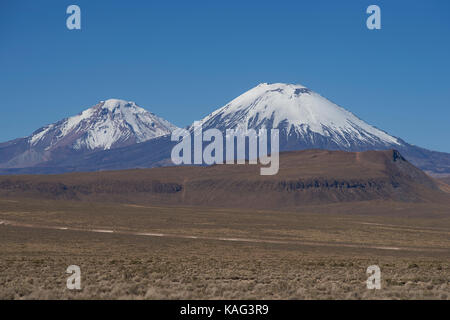 Coperte di neve vulcano parinacota (6342m) che sovrasta la altiplano e scogliere che corre lungo la valle del fiume lauca in lauca parco nazionale. Foto Stock