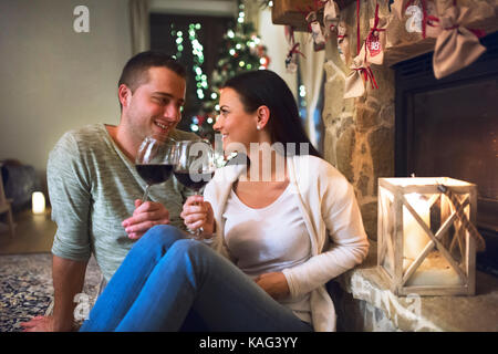 Giovane seduto di fronte al caminetto, bere vino. Foto Stock