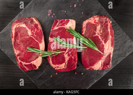 Tre fette di carne cruda su nero con il condimento Foto Stock