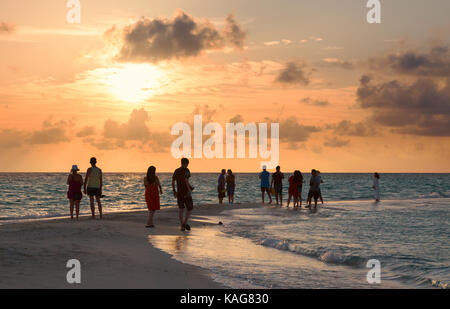 Maldive tramonto - la gente a guardare il tramonto sull'oceano indiano dalla spiaggia, Kuramathi island resort, Maldive Asia Foto Stock