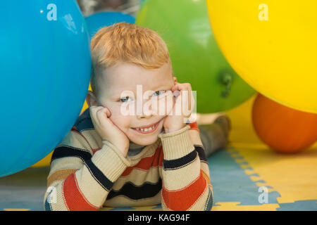 Un ragazzino sdraiato sul pavimento circondato da palloncino colorato Foto Stock