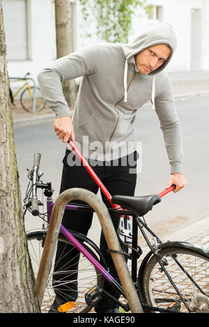 Ladro cercando di rompere il blocco di biciclette parcheggiate vicino alla strada Foto Stock