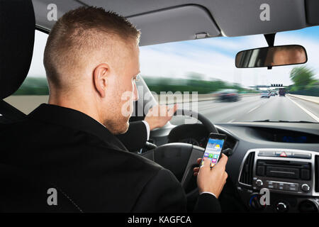 Vista posteriore di un imprenditore utilizzando il cellulare mentre si guida auto Foto Stock