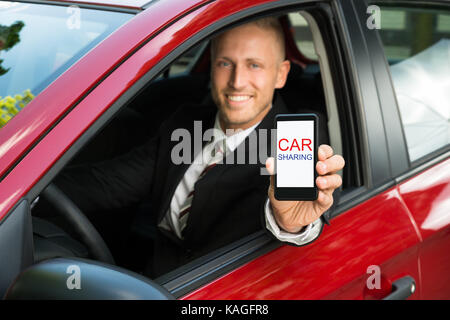 Happy businessman seduto in macchina che mostra il cellulare con il car sharing il testo sullo schermo Foto Stock
