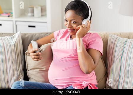 Donna incinta nelle cuffie con lo smartphone Foto Stock