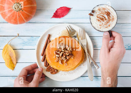 Frittelle di zucca con noci pecan e sciroppo d'acero, la crema di latte e cannella e la tazza di zucca spice latte. persona che mangia il cibo in autunno la prima colazione Foto Stock