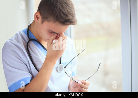 Ritratto di infelice stanco giovane medico avente mal di testa in prossimità di una finestra Foto Stock