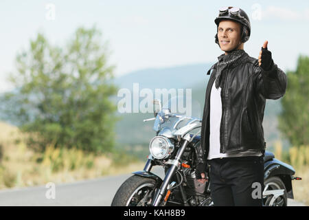 Biker rendendo un pollice in alto gesto nella parte anteriore di una motocicletta in esterno Foto Stock